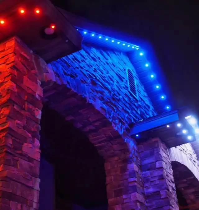 Color-changing permanent roofline lighting on a stone home at night